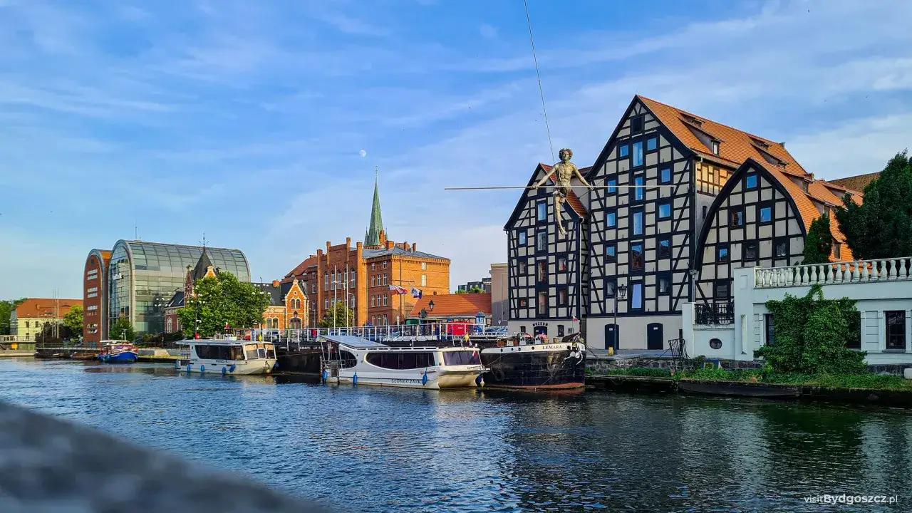 Bydgoszcz atrakcje: łodzie cumujące przy Wyspie Młyńskiej, z charakterystycznym akrobatą na linie nad kamieniczką.