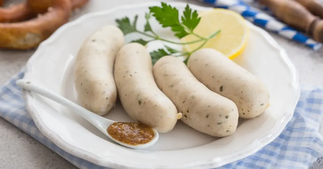 Cztery białe kiełbaski na talerzu z musztardą, cytryną i pietruszką. Zastanawiasz się nad biała kiełbasa kcal?
