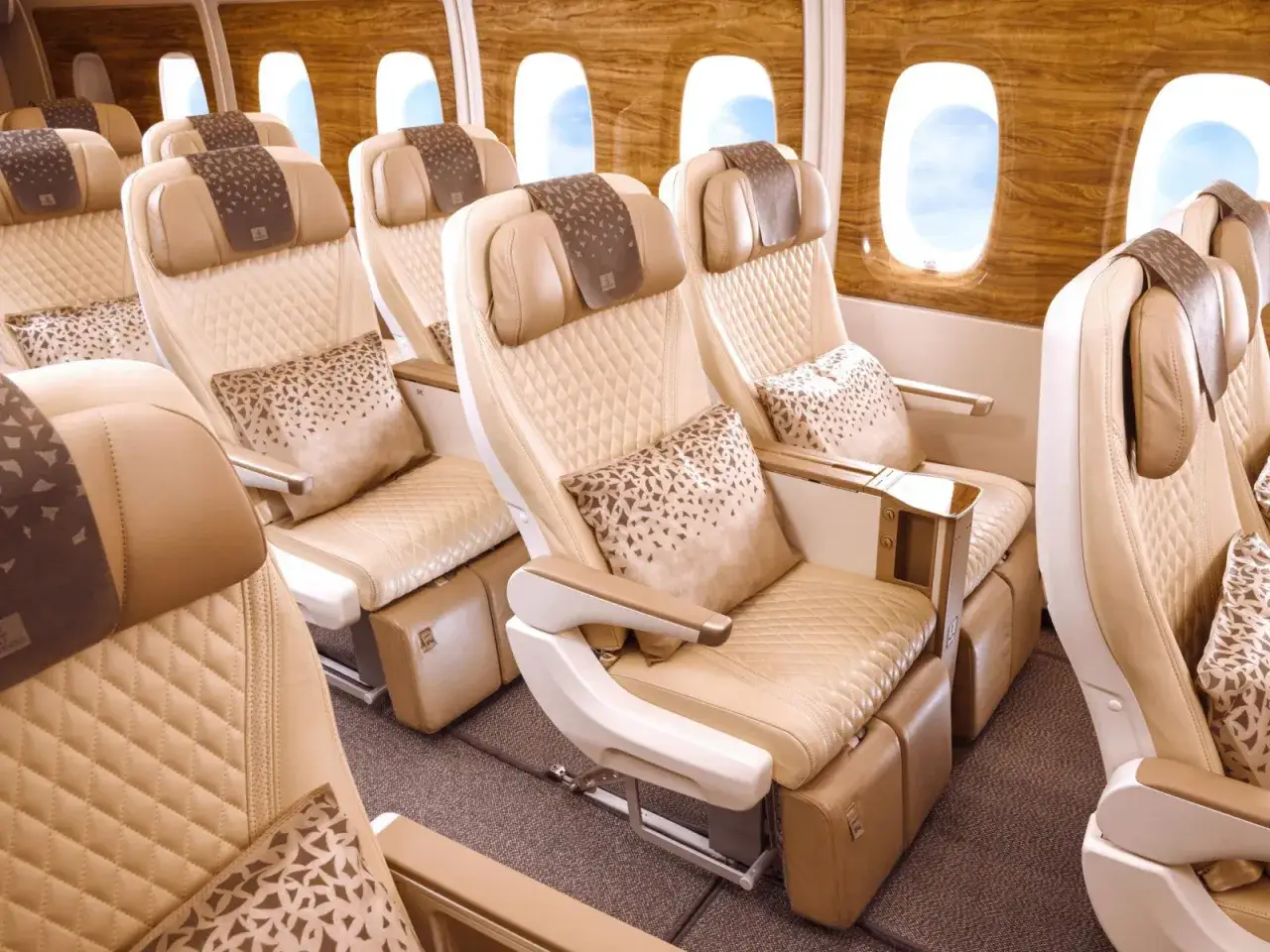 Luksusowe fotele lot premium economy w jasnych kolorach, z poduszkami i widokiem na niebo przez okna.