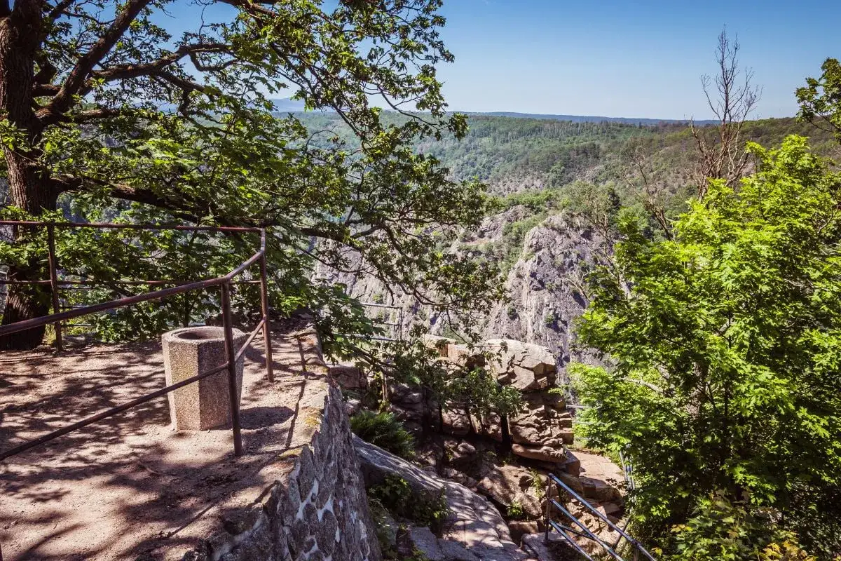 Ein Weg führt durch das Bodetal, vorbei an einem steinernen Abfallbehälter und einer Mauer, hinunter in die felsige Schlucht.
