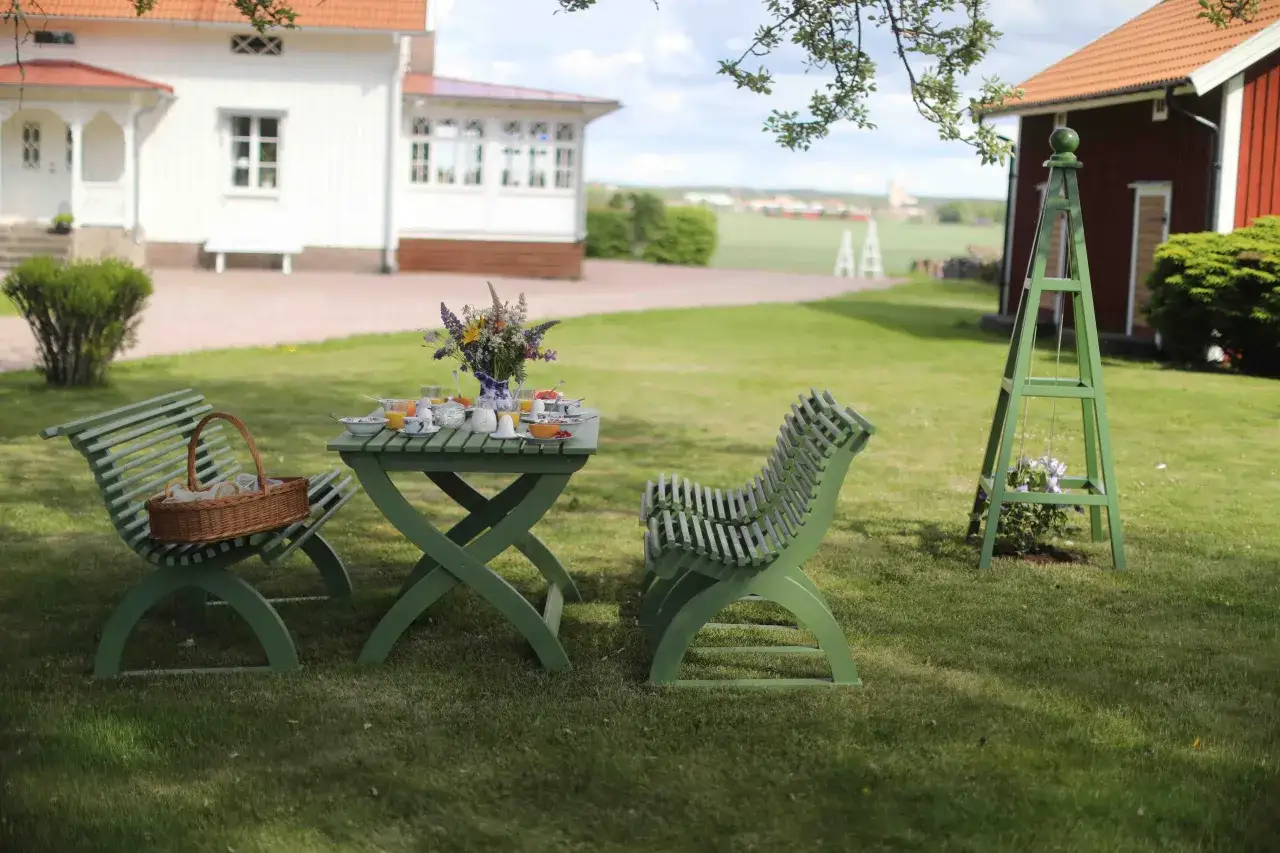 En grön rosentorn ritning står i en trädgård med ett frukostbord uppdukat.