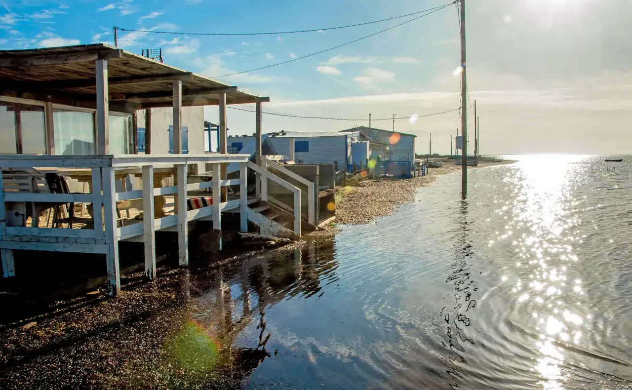 Vue d'une cabane de p&ecirc;cheur au bord de l'eau, avec des reflets du soleil sur la mer.