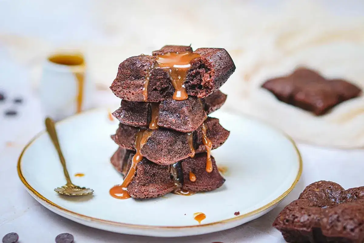 Pile de fondants au chocolat arrosés de caramel coulant. Une cuillère dorée repose sur l'assiette.