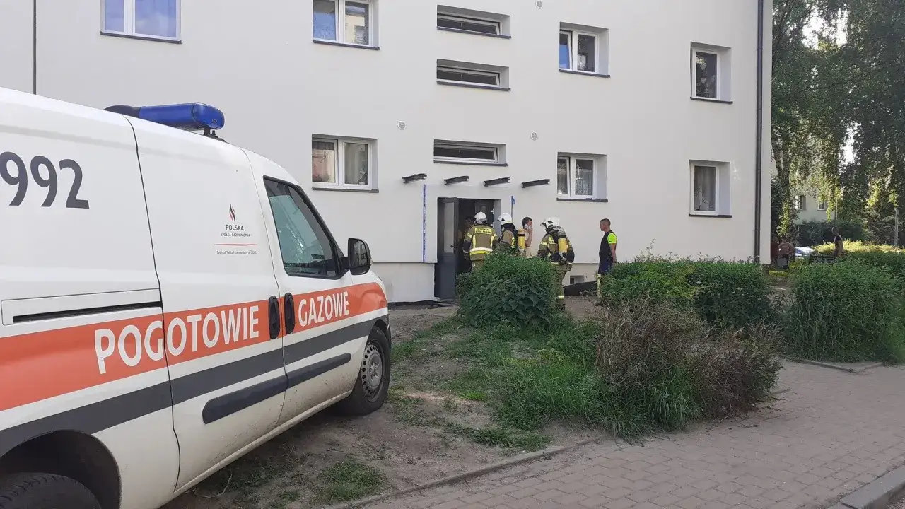 Pogotowie gazowe przy bloku, gdzie pracownicy w strojach ochronnych wchodzą do klatki schodowej.