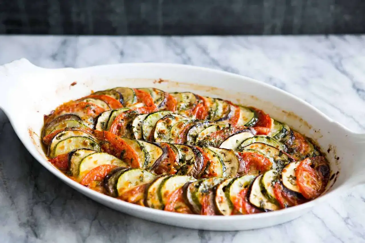 En vacker ugnsform med skivad aubergine, tomat och zucchini, perfekt för ett utsökt aubergine recept.