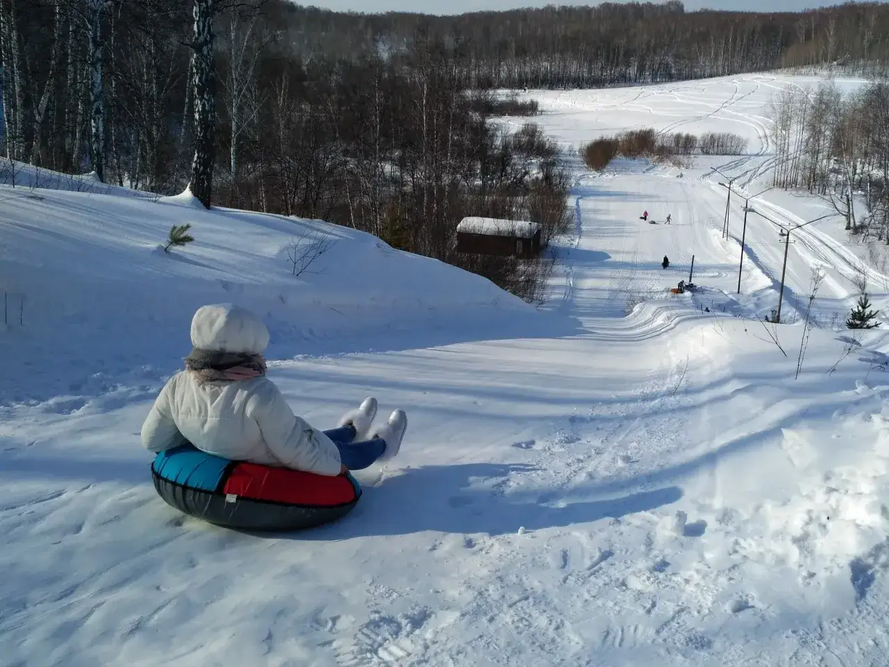 Dziecko na pontonie zjeżdża ze śnieżnej górki w szwajcaria bałtowska snowpark. W tle las i inni bawiący się na śniegu.