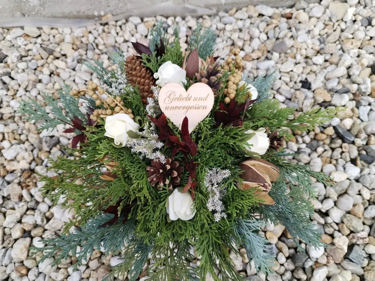 Ein Gesteck mit Tannenzweigen, wei&szlig;en Rosen und Zapfen, das als Totensonntag Symbol dient. Ein Herz mit der Aufschrift 