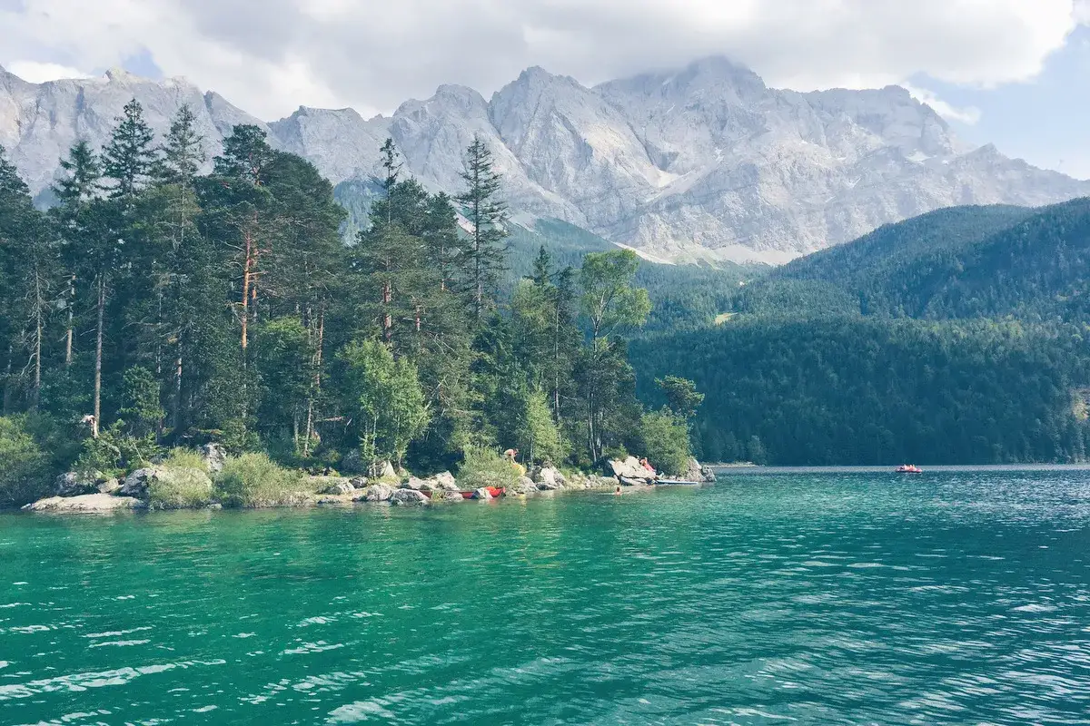 T&uuml;rkises Wasser am Eibsee Bayern, umgeben von gr&uuml;nen W&auml;ldern und majest&auml;tischen Bergen. Ein paar Boote sind auf dem See zu sehen.