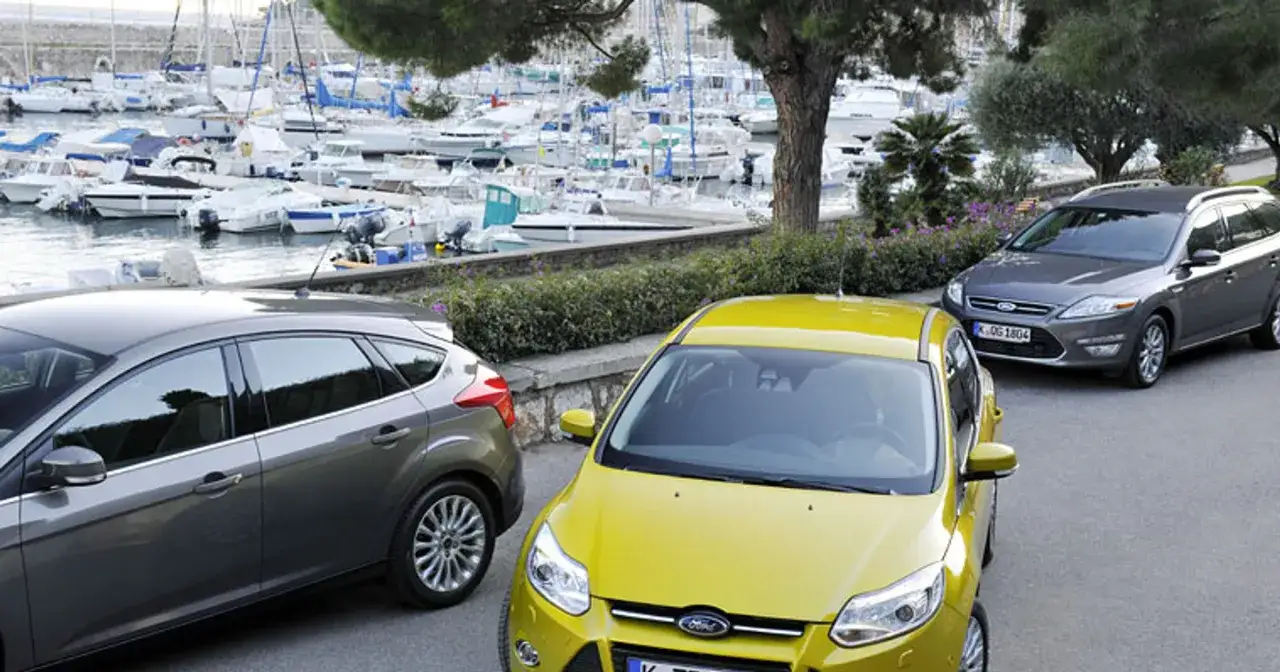 Dwa samochody, żółty Ford Focus 2 i szary Ford Mondeo, stoją przy nabrzeżu pełnym łodzi.