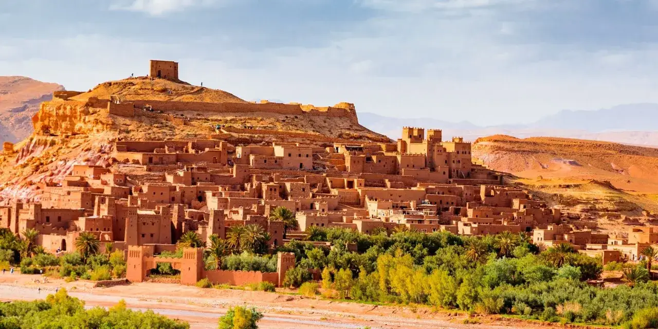 Ait Ben Haddou, starożytna kasba w Maroku, wznosi się na wzg&oacute;rzu, otoczona zielenią i pustynnym krajobrazem.