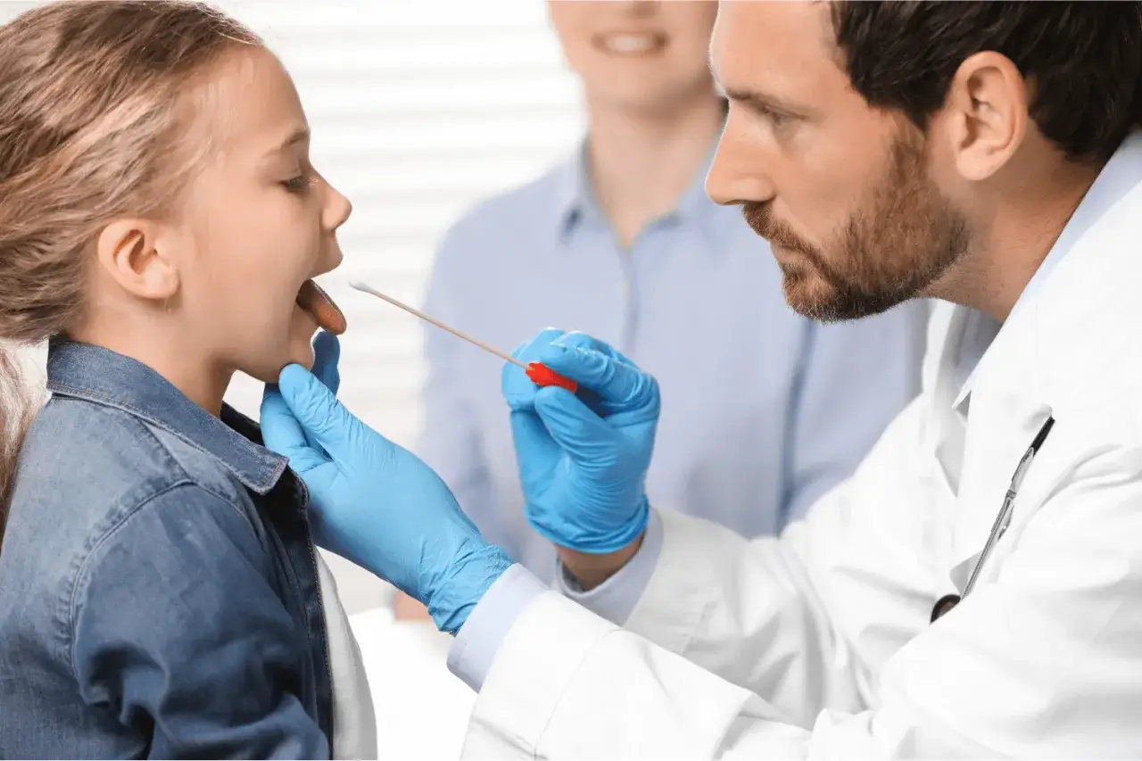 Medico esegue tampone faringeo per diagnosticare faringite da streptococco a bambina, con genitore sullo sfondo.
