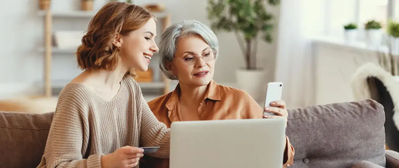 Dwie kobiety na kanapie korzystają z laptopa i telefonu. Młodsza trzyma kartę, starsza smartfon. Czy kasa stefczyka to bank?