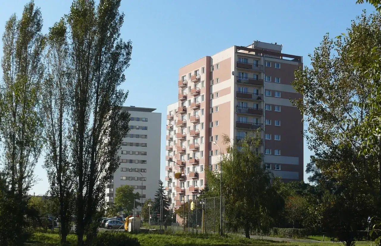 Wysokie bloki mieszkalne na osiedlu Lotnictwa Polskiego, otoczone zielenią i drzewami.