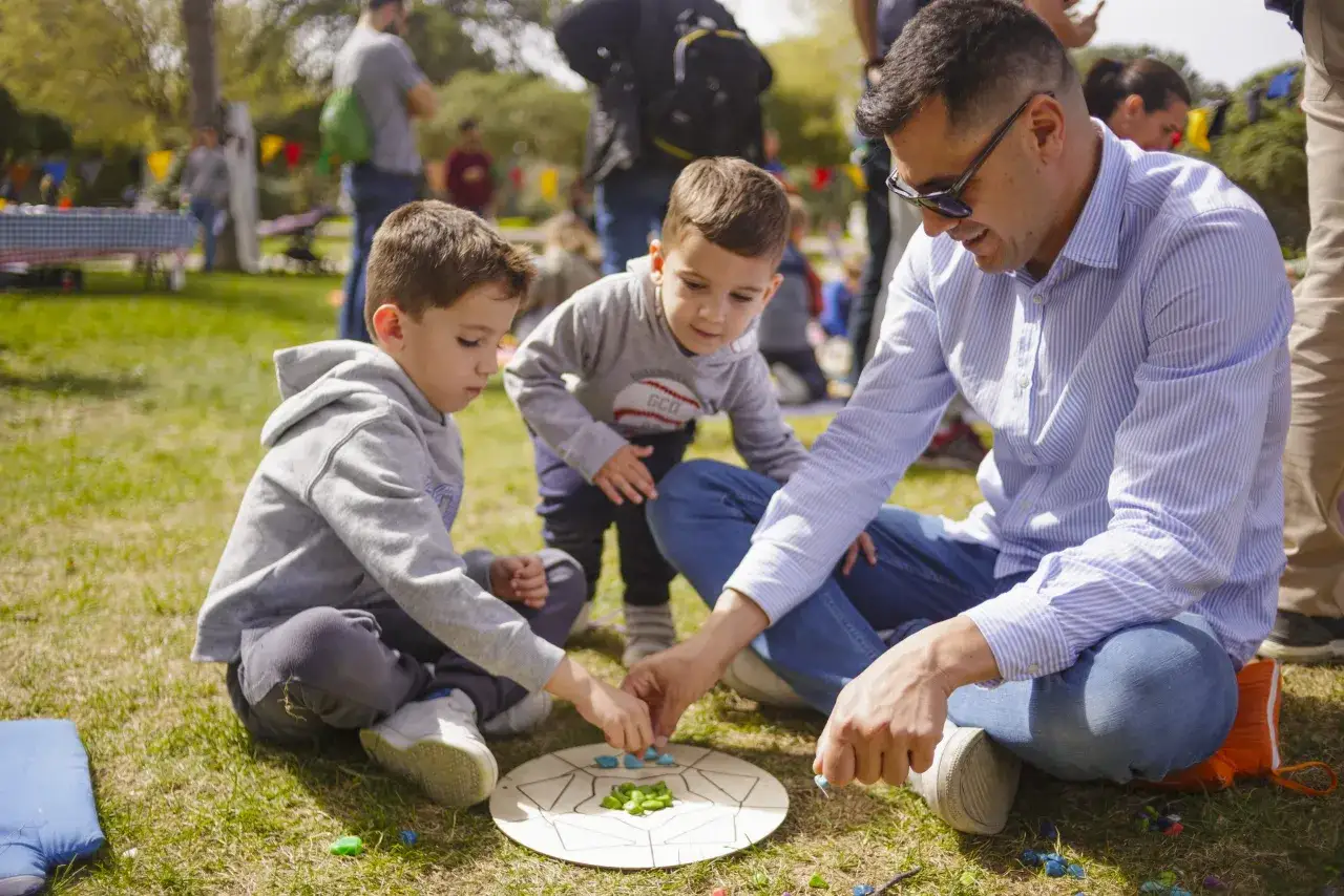 Un padre juega con sus hijos en el parque Zaragoza, creando un mandala con piedras de colores.