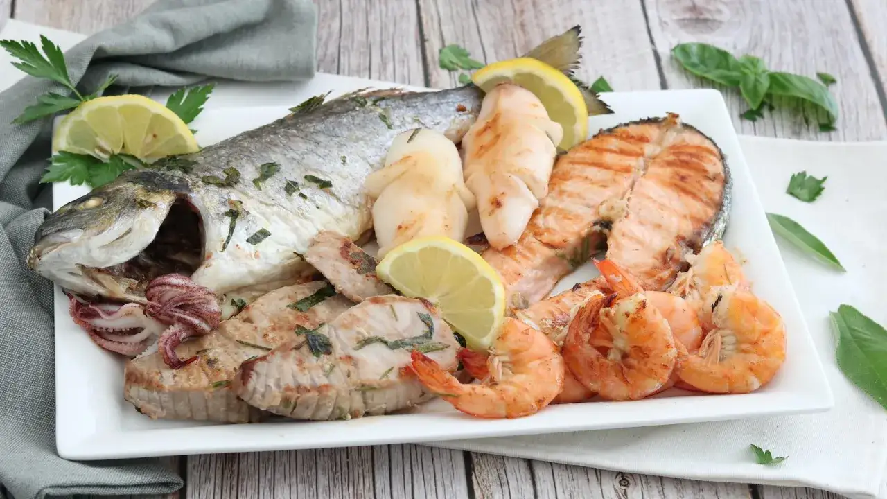 Un invitante piatto di grigliata di pesce con orata, salmone, gamberi, calamari e tonno, guarnito con limone e prezzemolo.