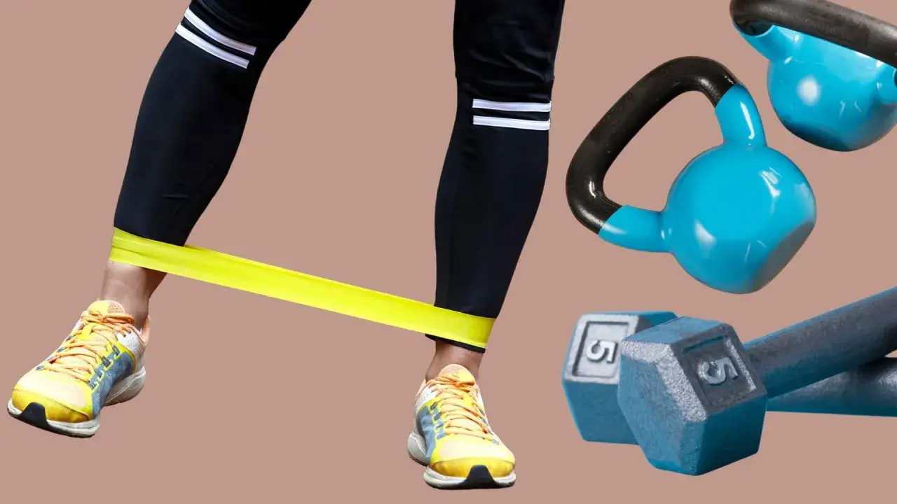 Noga w żółtej taśmie oporowej, obok niebieskie kettlebells i hantle. Efektywny trening oporowy w domu.