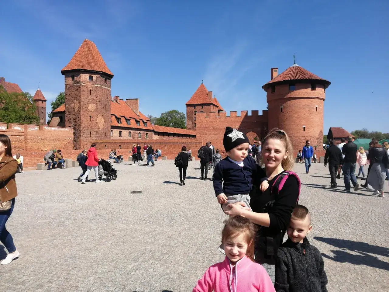 Rodzina zwiedza zamek w Malborku, szukając atrakcji dla dzieci. Dzieci zachwycone potęgą ceglanych mur&oacute;w.