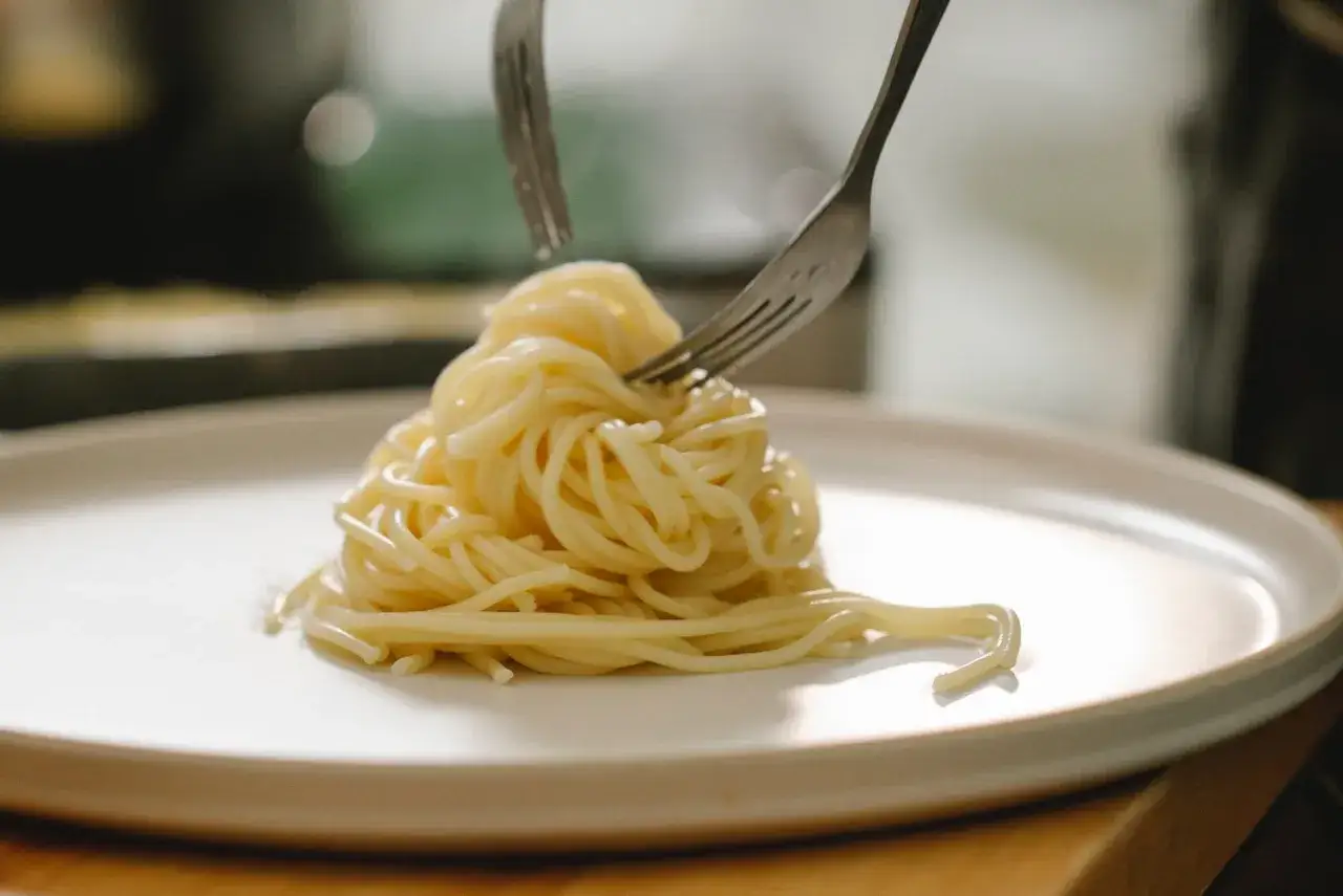 Spaghetti al limone serviti su un piatto bianco, con due forchette che raccolgono la pasta.