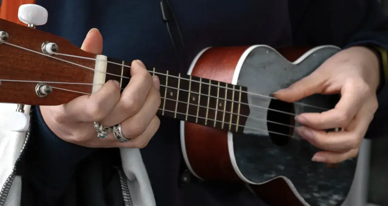 H&auml;nde spielen auf einem Ukulele, einem kleinen Saiteninstrument.