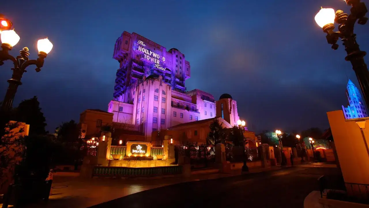 La Hollywood Tower Hotel de Disneyland Paris se ilumina de púrpura bajo el cielo nocturno, invitando a la aventura.