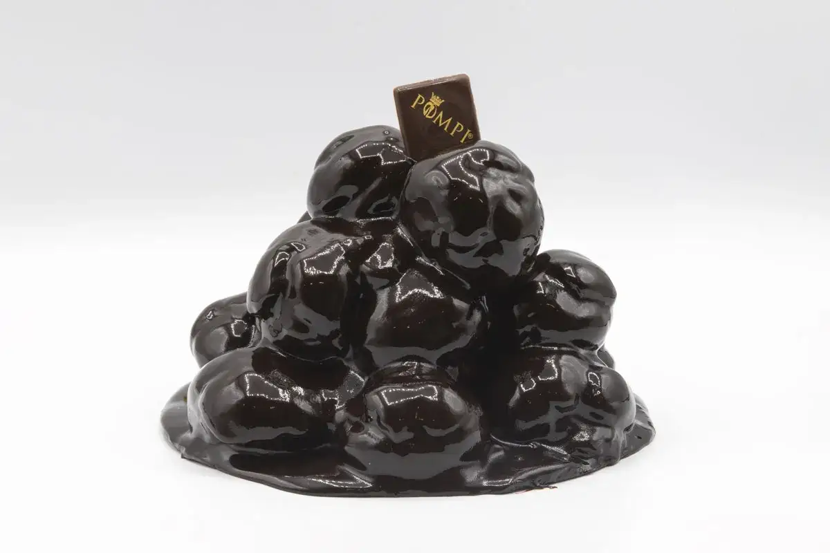Una piramide di bignè ricoperti di cioccolato lucido, perfetta per un compleanno. La torta profitterol è decorata con un quadratino di cioccolato con il logo