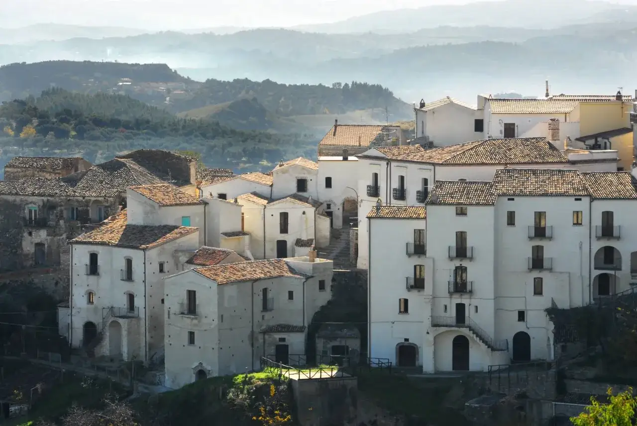 Un borgo arroccato tra le colline nebbiose, dove sembra che Cristo si sia fermato a Eboli, con case bianche e tetti rossi che si stagliano nel paesaggio.