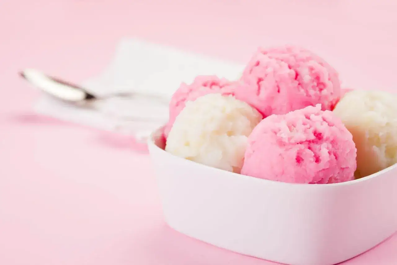 Miseczka z różowymi i białymi gałkami lodów. Czy to sorbet owocowy czy lody mleczne? Obok leży łyżeczka.
