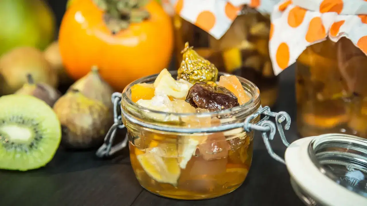 Frutas confitadas en un frasco, con higos, naranjas y otros frutos. Esto es mostarda que es una conserva dulce.