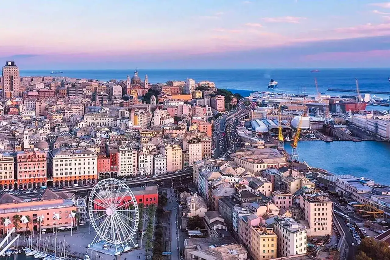 Vue panoramique de Gênes au coucher du soleil. Une grande roue domine le port animé. Que faire à Gênes ? Explorer cette ville portuaire colorée.