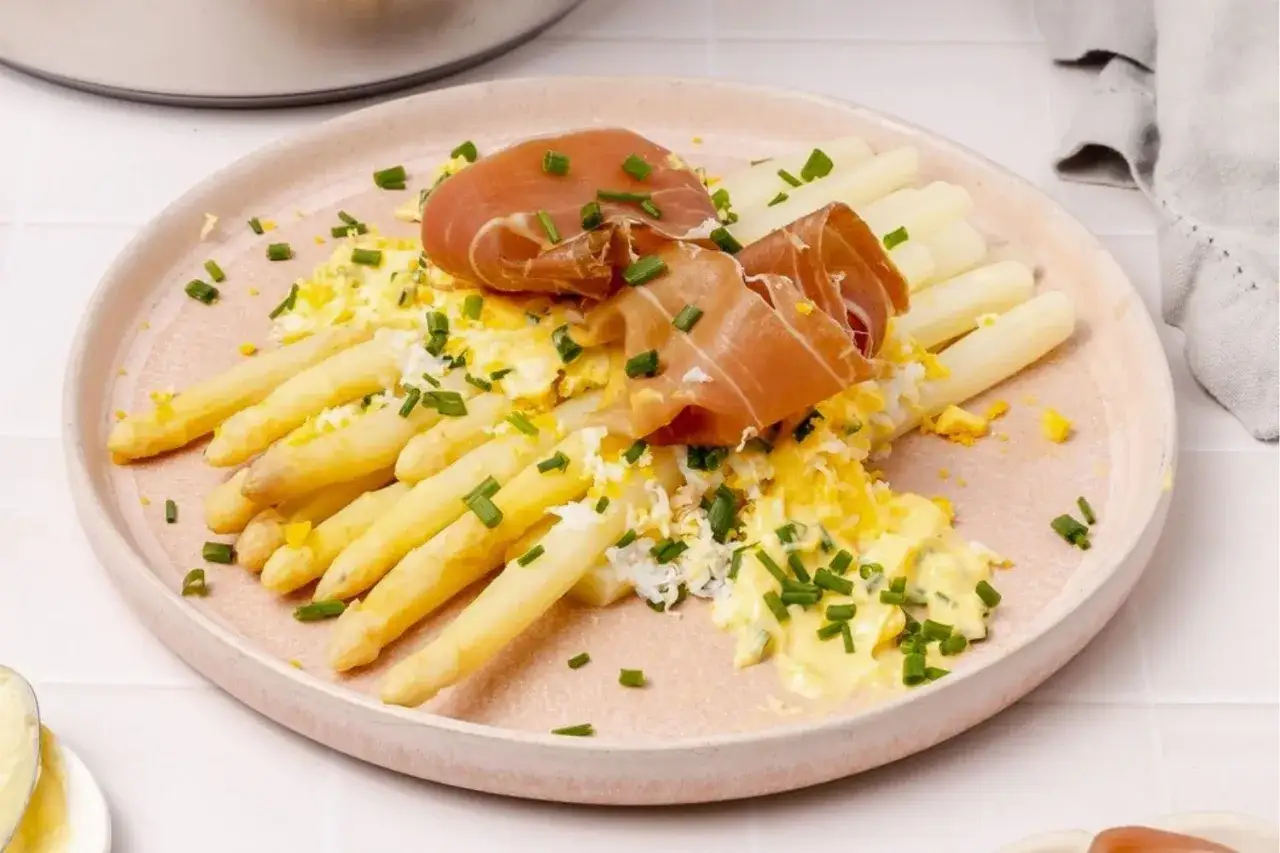 Asperges blanches servies avec une sauce crémeuse, des œufs brouillés, du jambon cru et de la ciboulette. Un délice printanier !