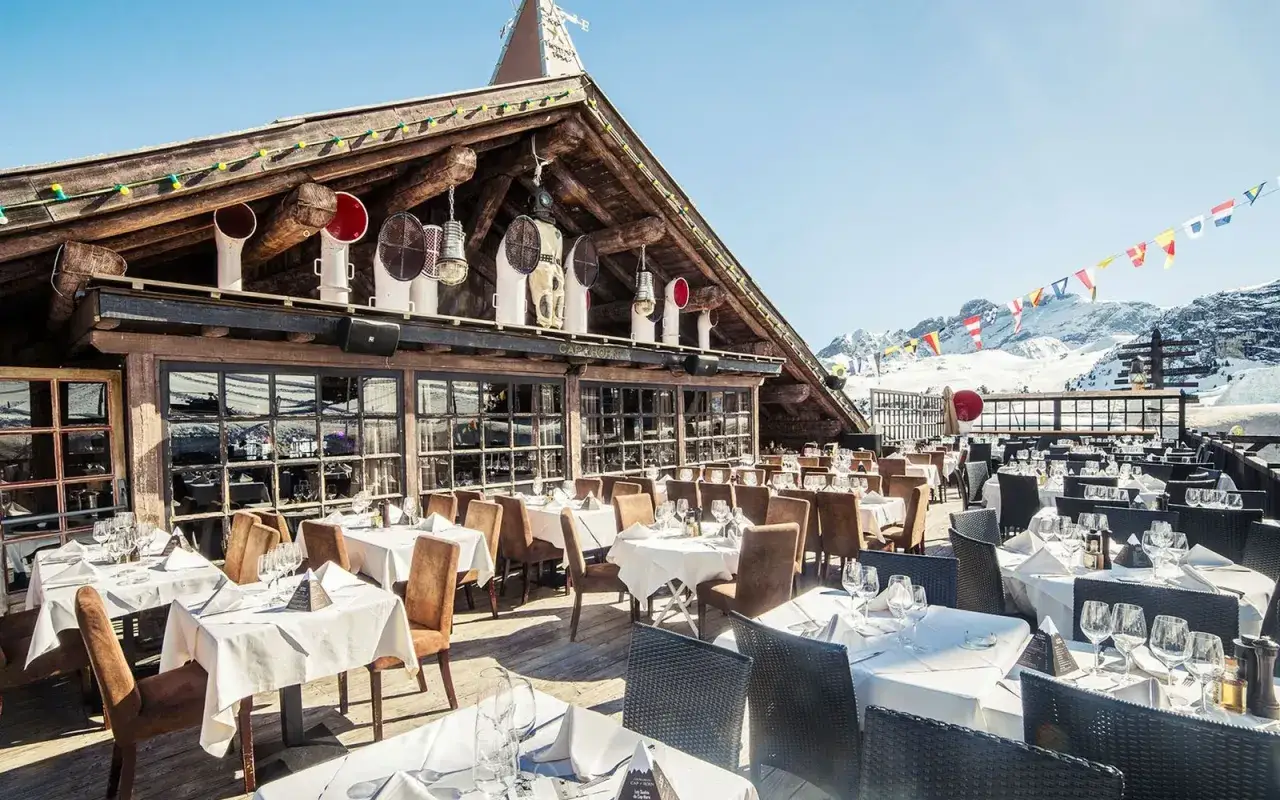 Terrasse de restaurants des Hautes-Alpes, tables dressées sous un ciel bleu, avec vue sur les montagnes enneigées.