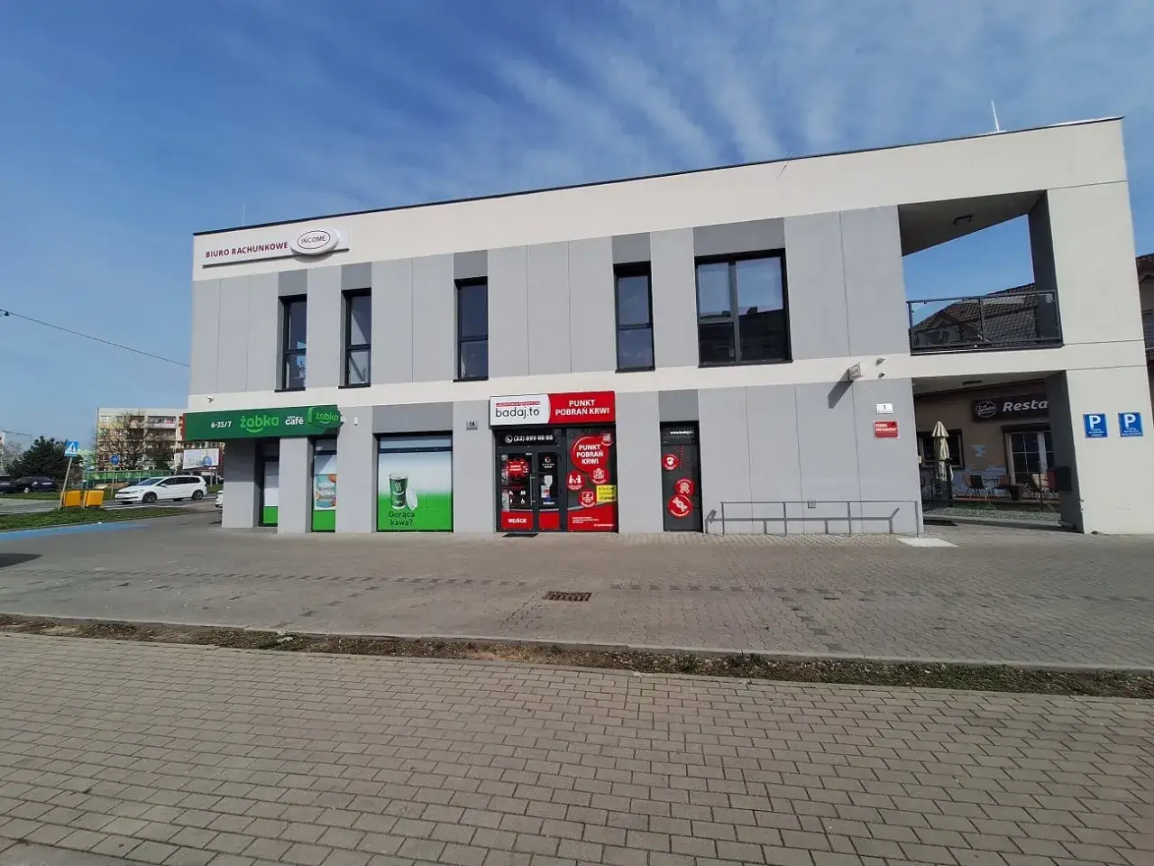 Budynek z szyldami: Biuro Rachunkowe, Żabka, badaj.to (punkt pobrań krwi) i restauracja. Ważne skierowanie na badania krwi.