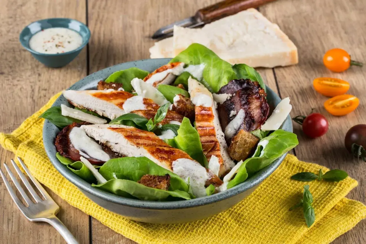 Pyszna sałatka cezar z boczkiem, grillowanym kurczakiem, grzankami i parmezanem, polana kremowym sosem.