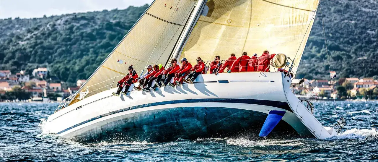 Segelboot mit Crew in roten Jacken, die auf der Reling sitzen. Tatjana Pokorny ist Teil dieses Teams, das &uuml;ber das Meer gleitet.