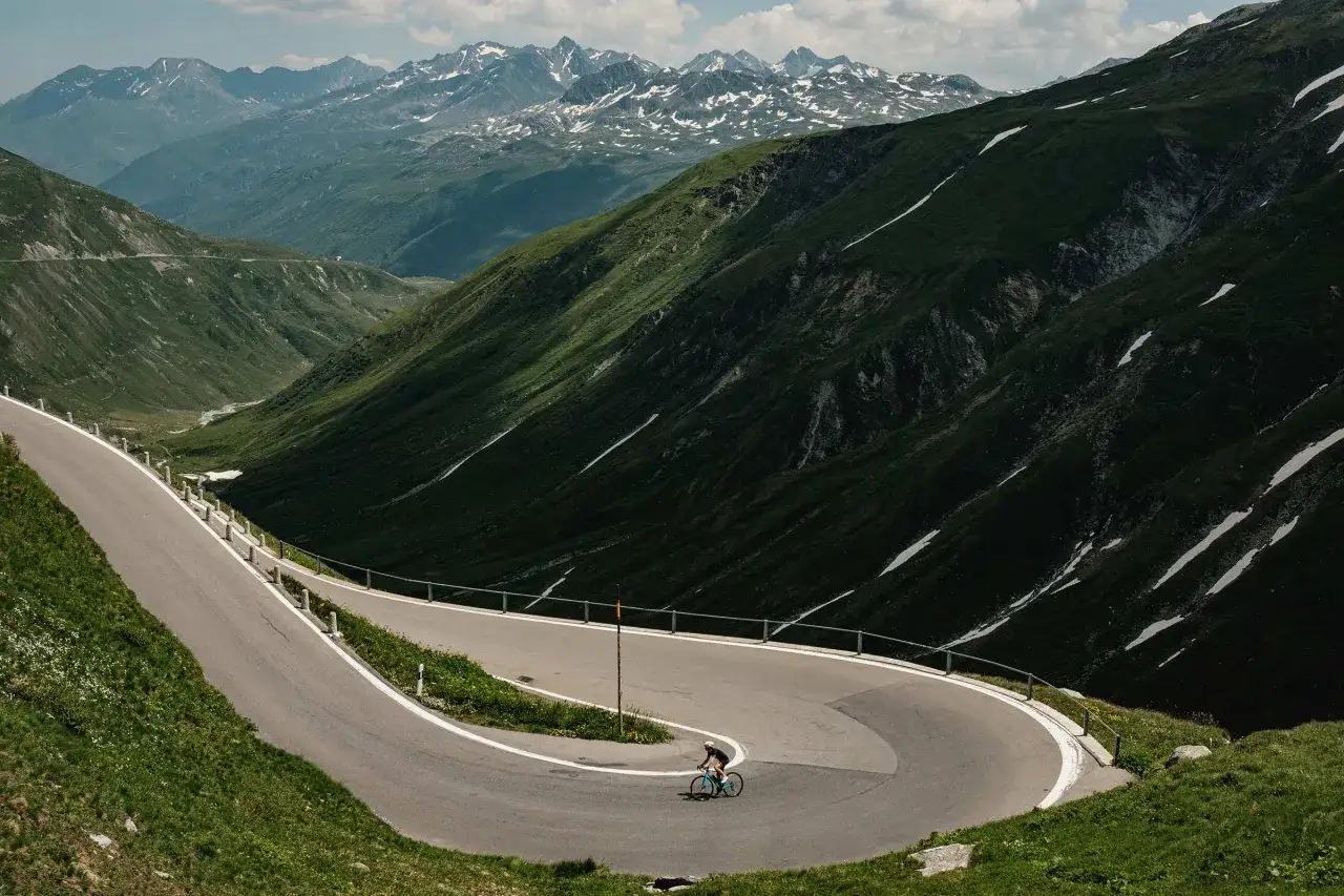 Radfahrer auf einem Transalp Rennrad meistert Serpentinen in den Alpen. Majest&auml;tische Bergkulisse mit Schneefeldern.