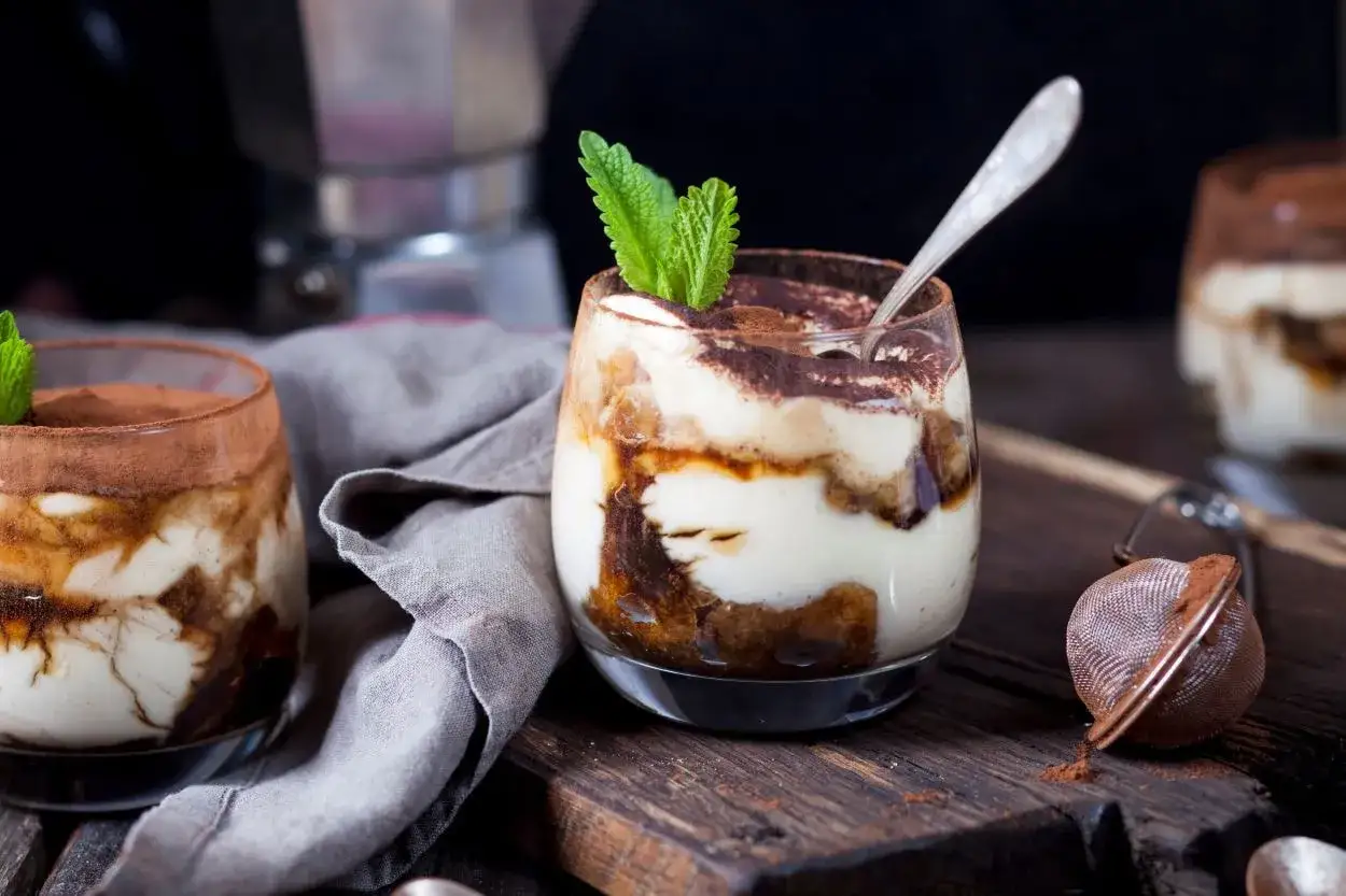 Pyszne tiramisu w pucharkach, udekorowane listkiem mięty, czeka na spróbowanie.