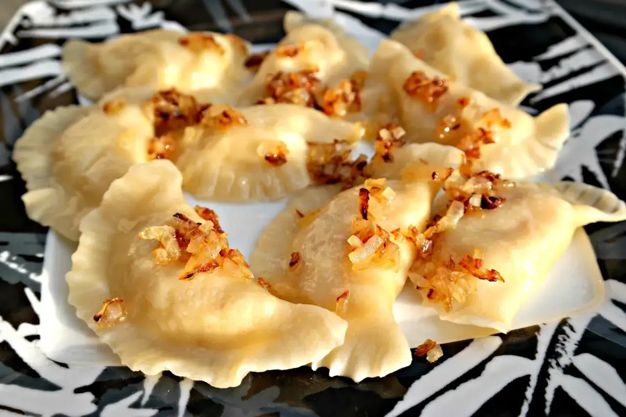 Pyszne pierogi ruskie przepis na talerzu, posypane skwarkami z cebulki.