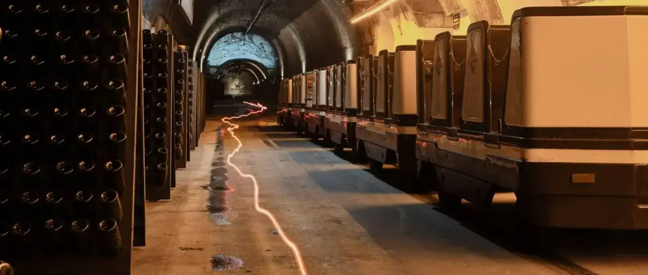 Dans une cave, des rangées de bouteilles en attente et des chariots évoquent le mystère de qu'est ce que le champagne.