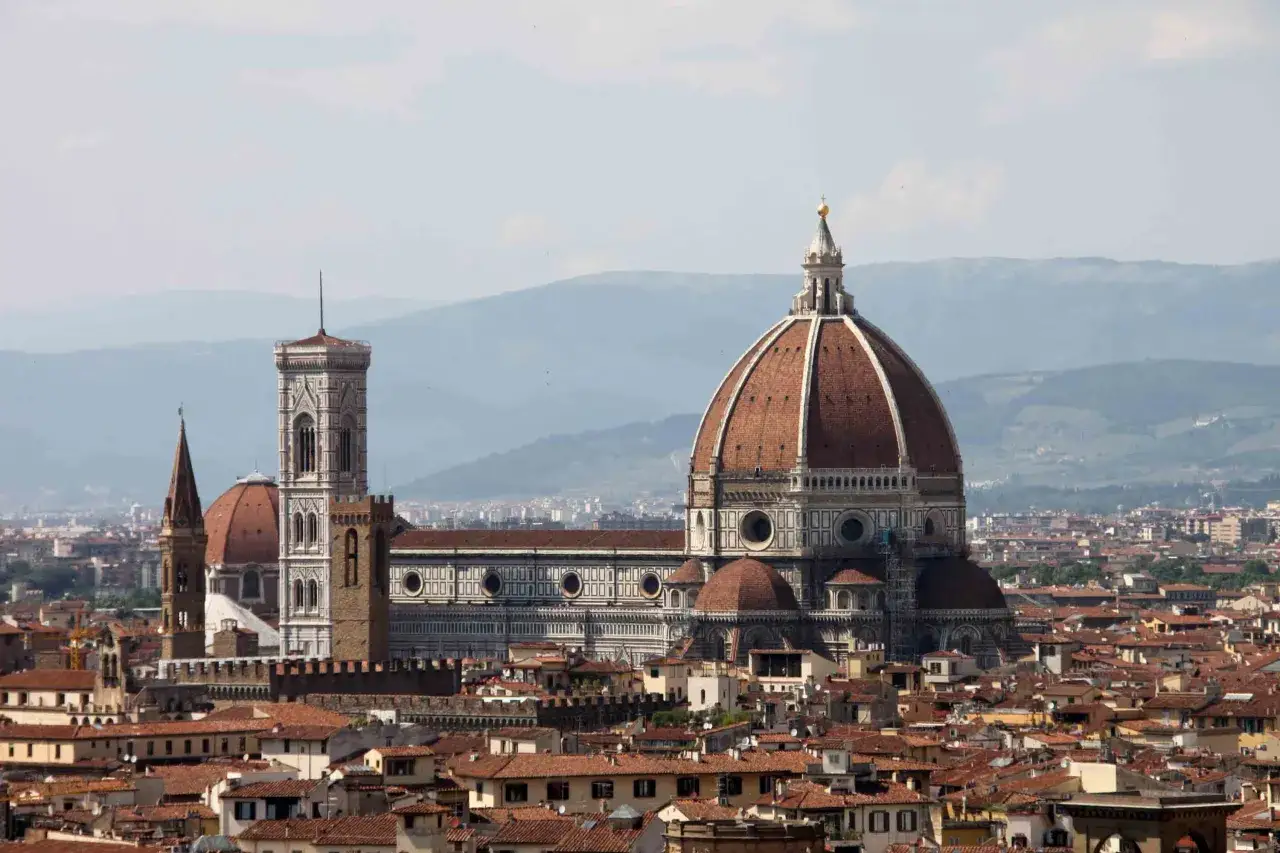 Vue panoramique de Florence, domin&eacute;e par la majestueuse **cattedrale Santa Maria** del Fiore et son d&ocirc;me embl&eacute;matique, se dressant au-dessus des toits de tuiles rouges.