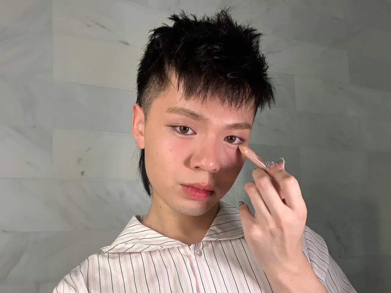 Joven aplicando corrector en el área de los ojos, parte de su rutina de maquillaje coreano para realzar la mirada.