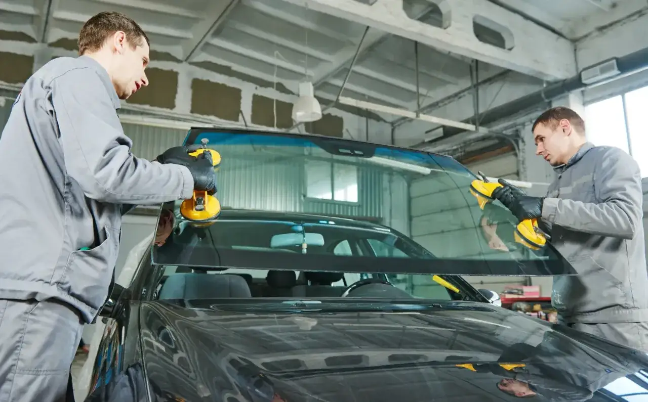 Dwóch mechaników wymienia przednią szybę w samochodzie. Dowiedz się, ile kosztuje naprawa odprysku na szybie.