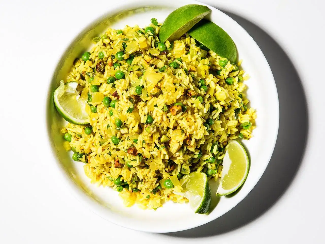 Un plato de arroz al curry con guisantes y trozos de lima.