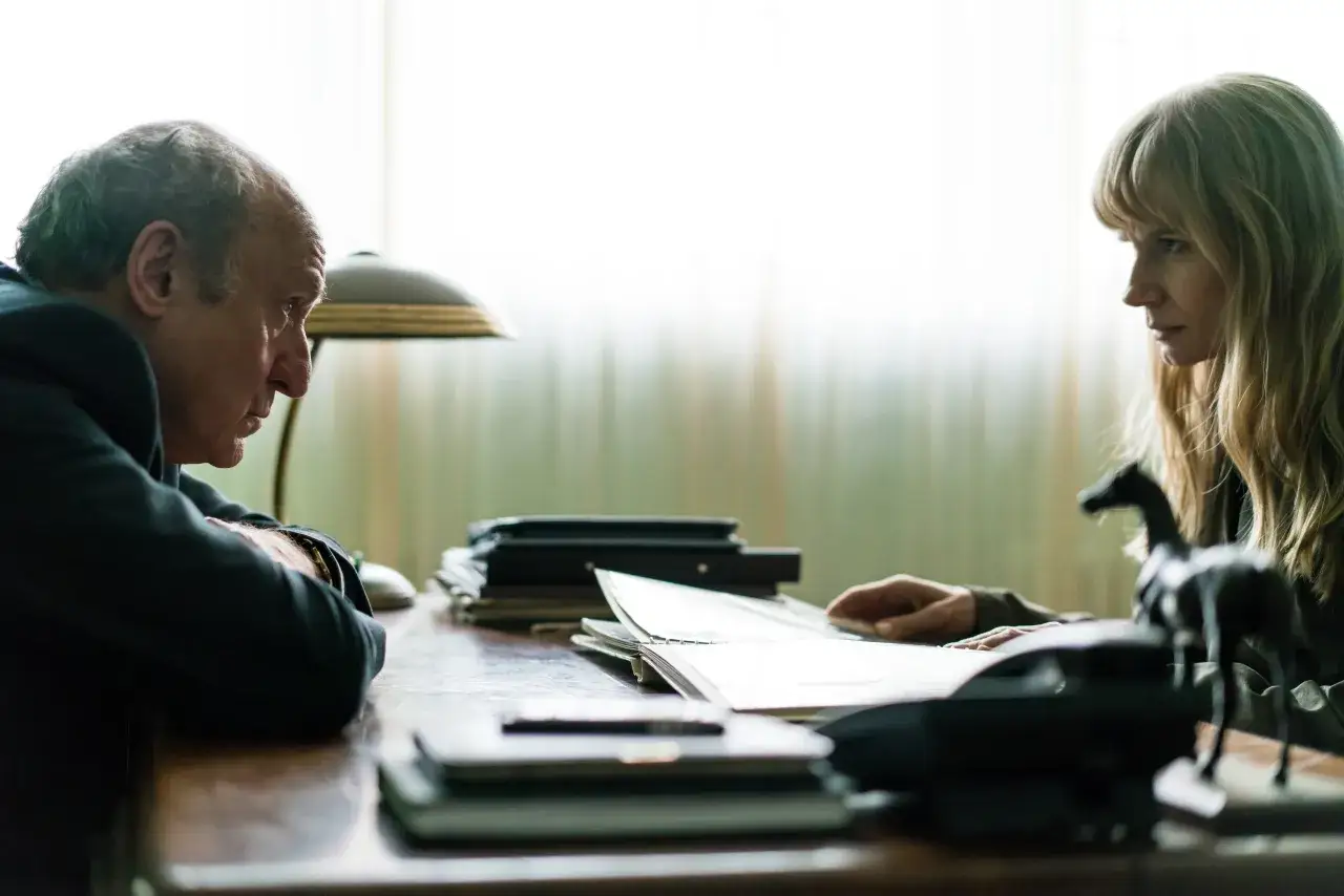 Mężczyzna i kobieta siedzą przy biurku, pochyleni nad dokumentami. Atmosfera sugeruje napięcie, jak w scenie z filmu