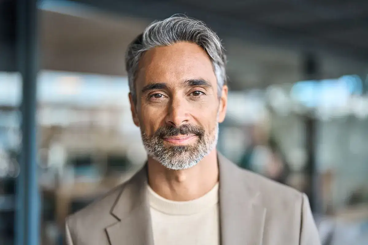 Hombre de mediana edad con pelo gris y barba, viste chaqueta y jersey.