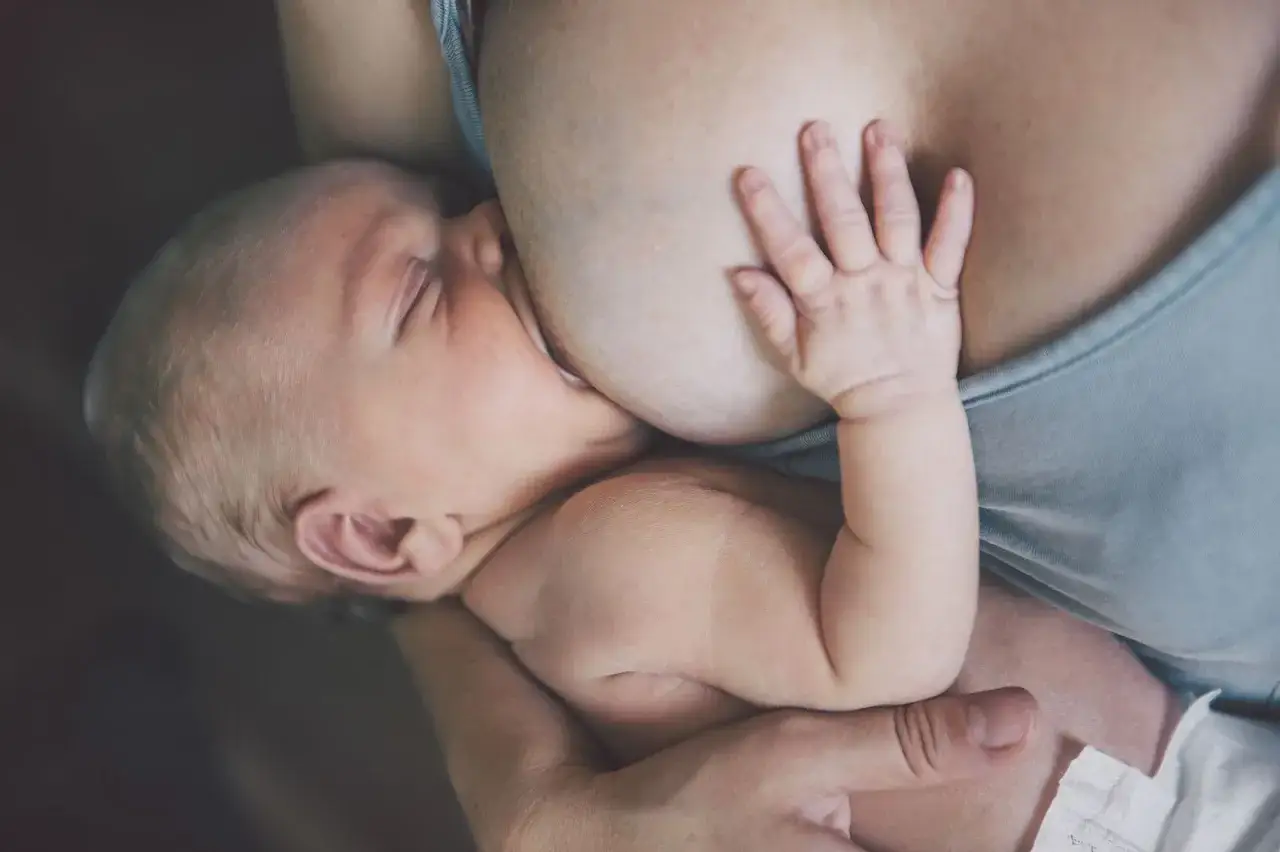 Noworodek karmiony piersią, jego mała rączka spoczywa na piersi mamy. To piękny moment bliskości i zaspokojenia, gdy pojawia się nawał pokarmu.