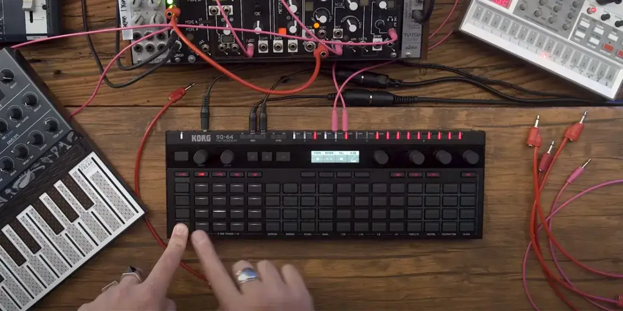 Ręce programują sekwencer Korg SQ-64, otoczony innymi modułami syntezator&oacute;w i kablami.