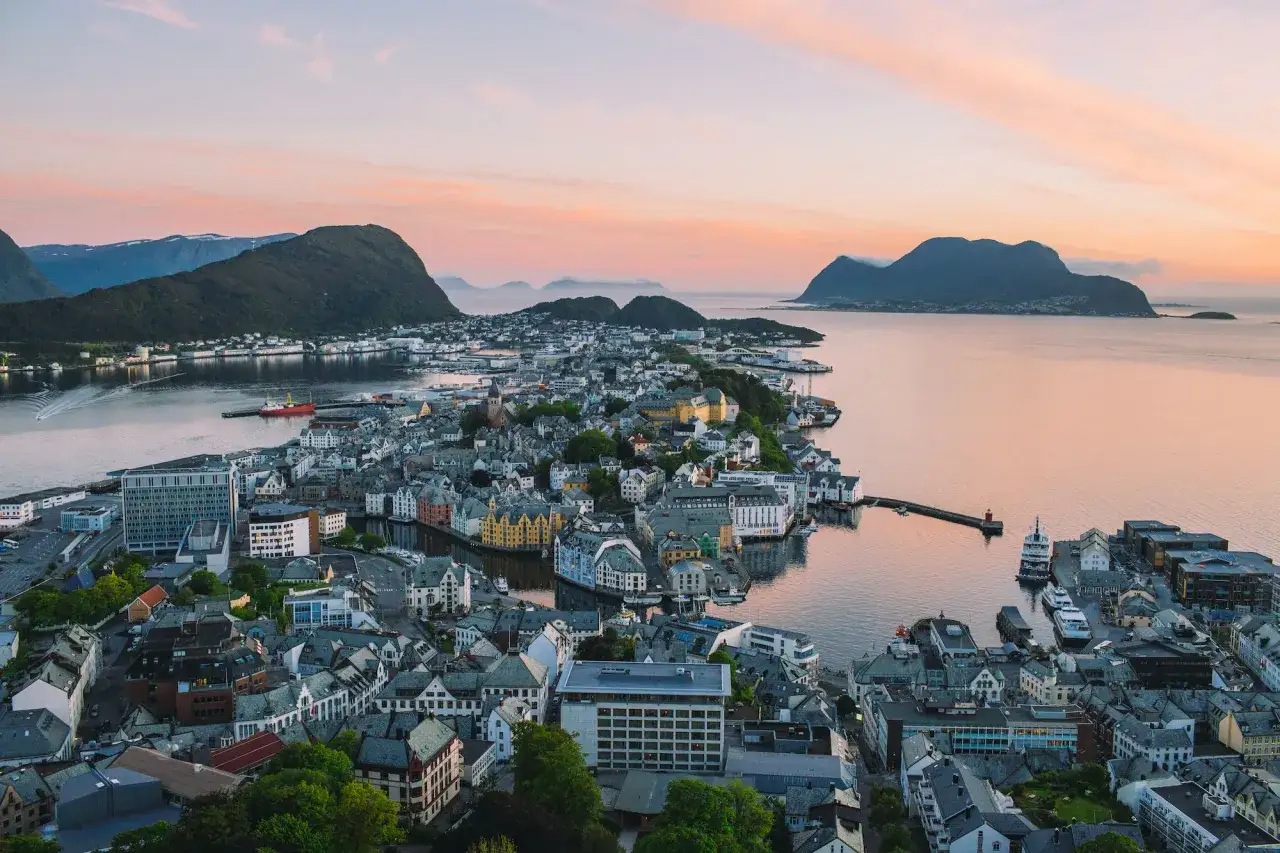 Vacker solnedgång över Ålesund, Norge, med sina färgglada hus och omgivande berg.
