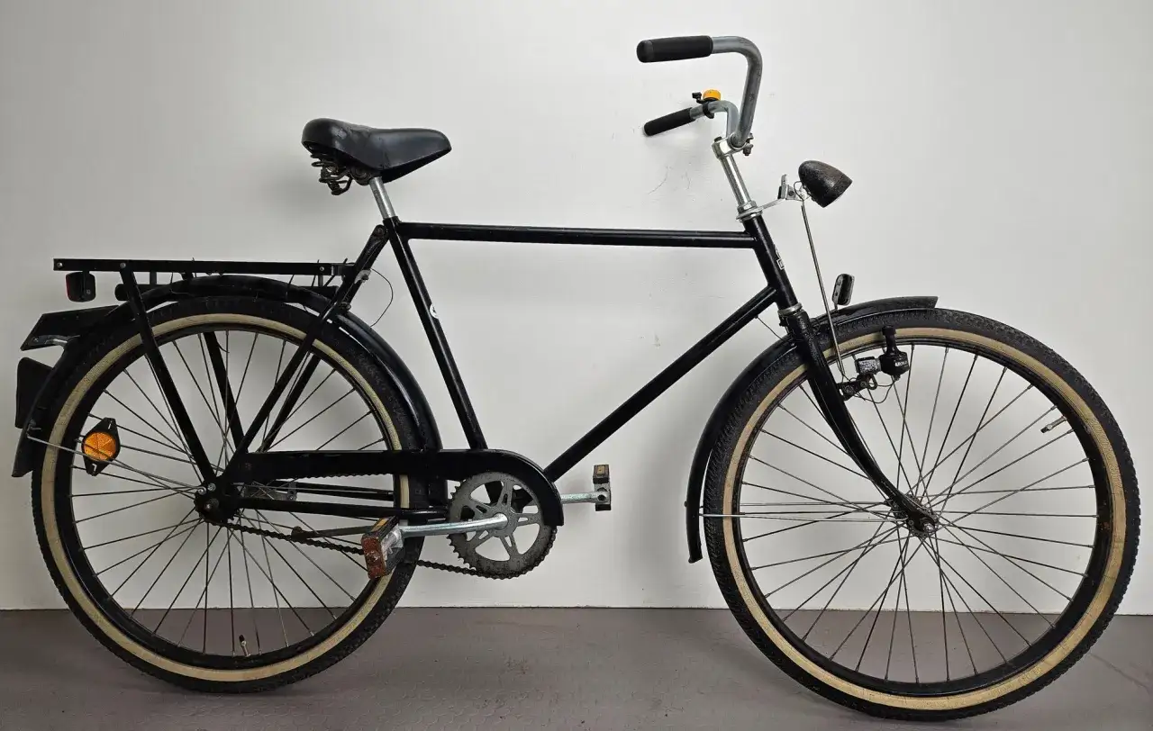 Svart cykel med paketh&aring;llare och klassiska d&auml;cksidor. Perfekt f&ouml;r dig som s&ouml;ker **kronan cykel reservdelar** f&ouml;r att h&aring;lla din trotj&auml;nare i toppskick.