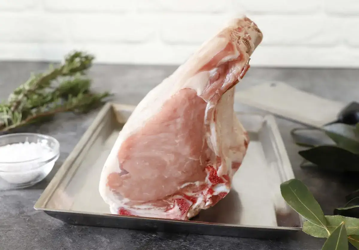 Una succulenta costata di vitello cruda, pronta per essere cucinata, su un vassoio metallico con rosmarino e sale.