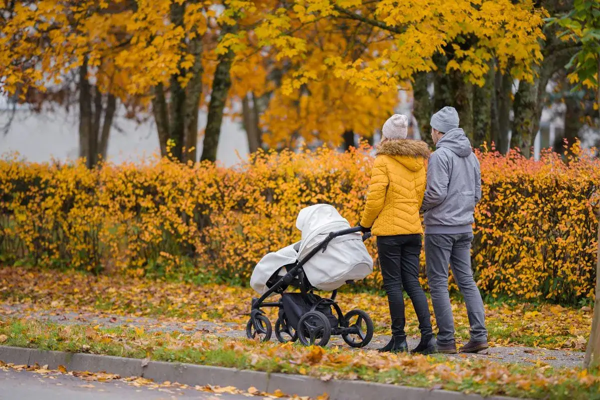 Spacer z wózkiem w złotej jesieni. Rodzice w ciepłych kurtkach i czapkach cieszą się pierwszym dniem jesieni, spacerując pośród kolorowych liści.